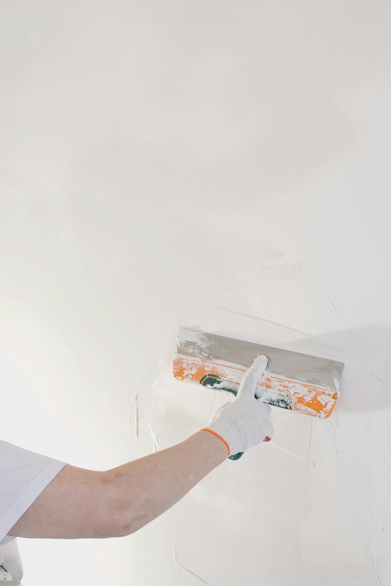 Close-up of a gloved hand plastering a wall with a spatula in a home renovation setting.