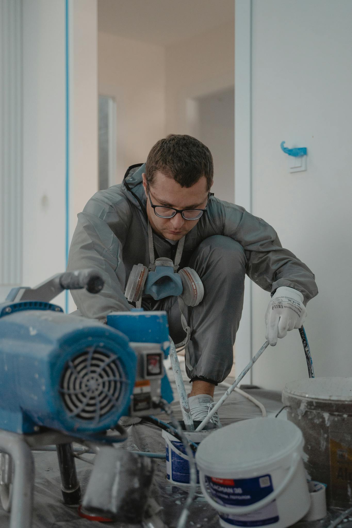 Man painting indoors for a home renovation project using protective gear and paint sprayer.